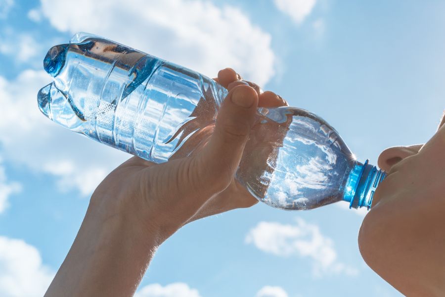 Someone drinking a water bottle outside with the sun shining through it